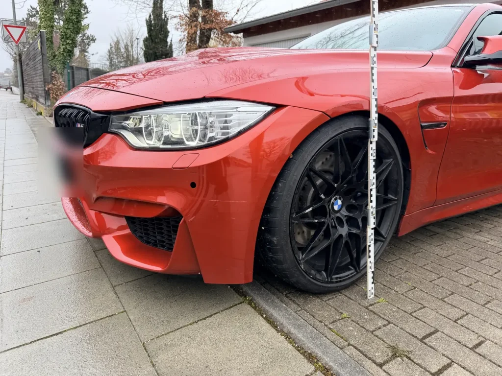 Frontschaden an einem roten Sportwagen, mit Messlatte dokumentiert